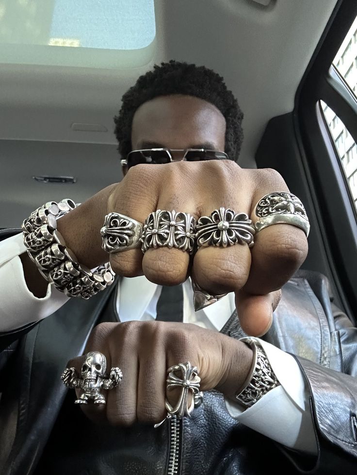 Man sitting in a car, displaying hands adorned with bold silver rings, showcasing unique style.